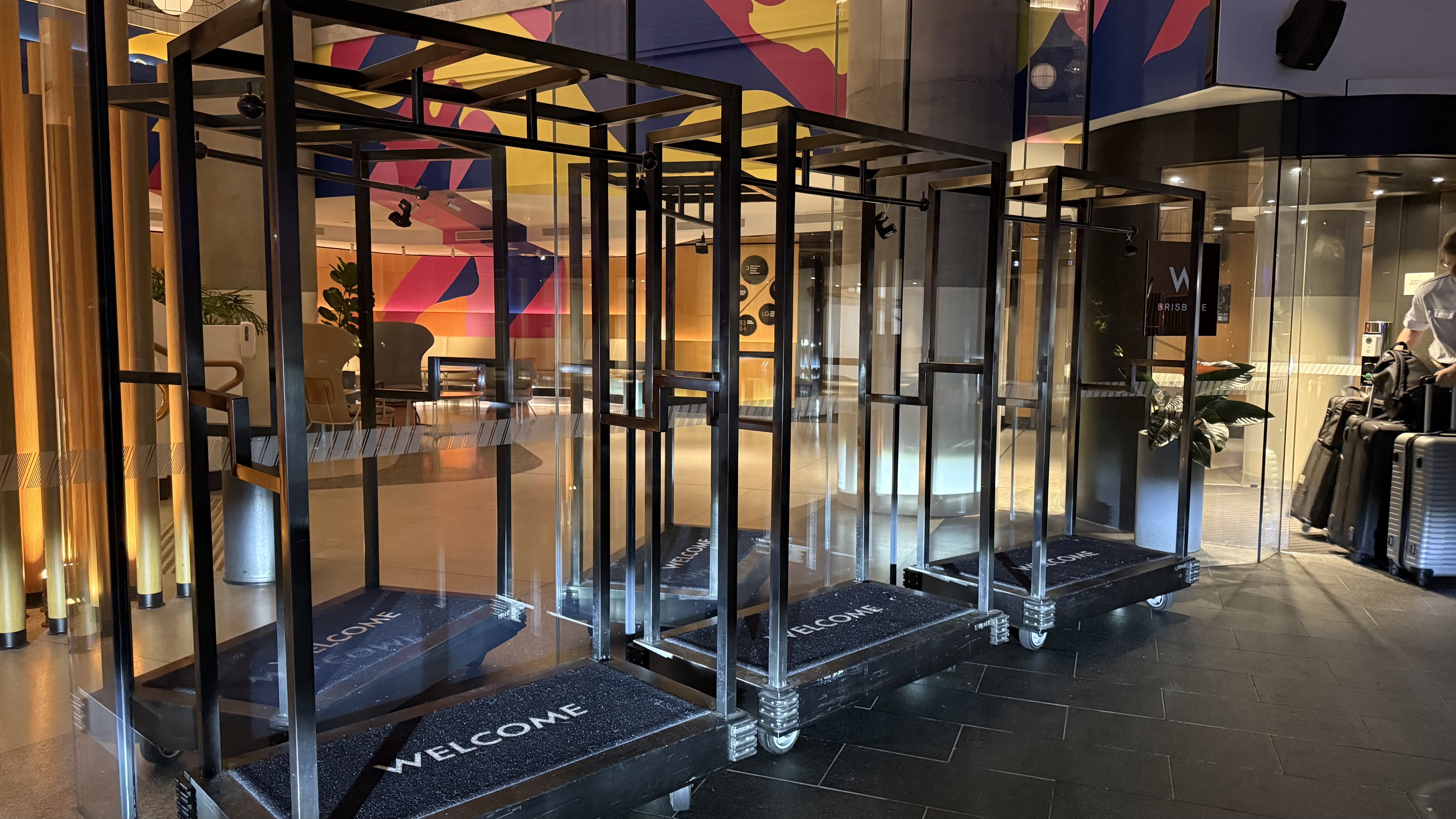 W Brisbane entrance — luggage trolleys lined with "Welcome" mats and the vivid mural beyond