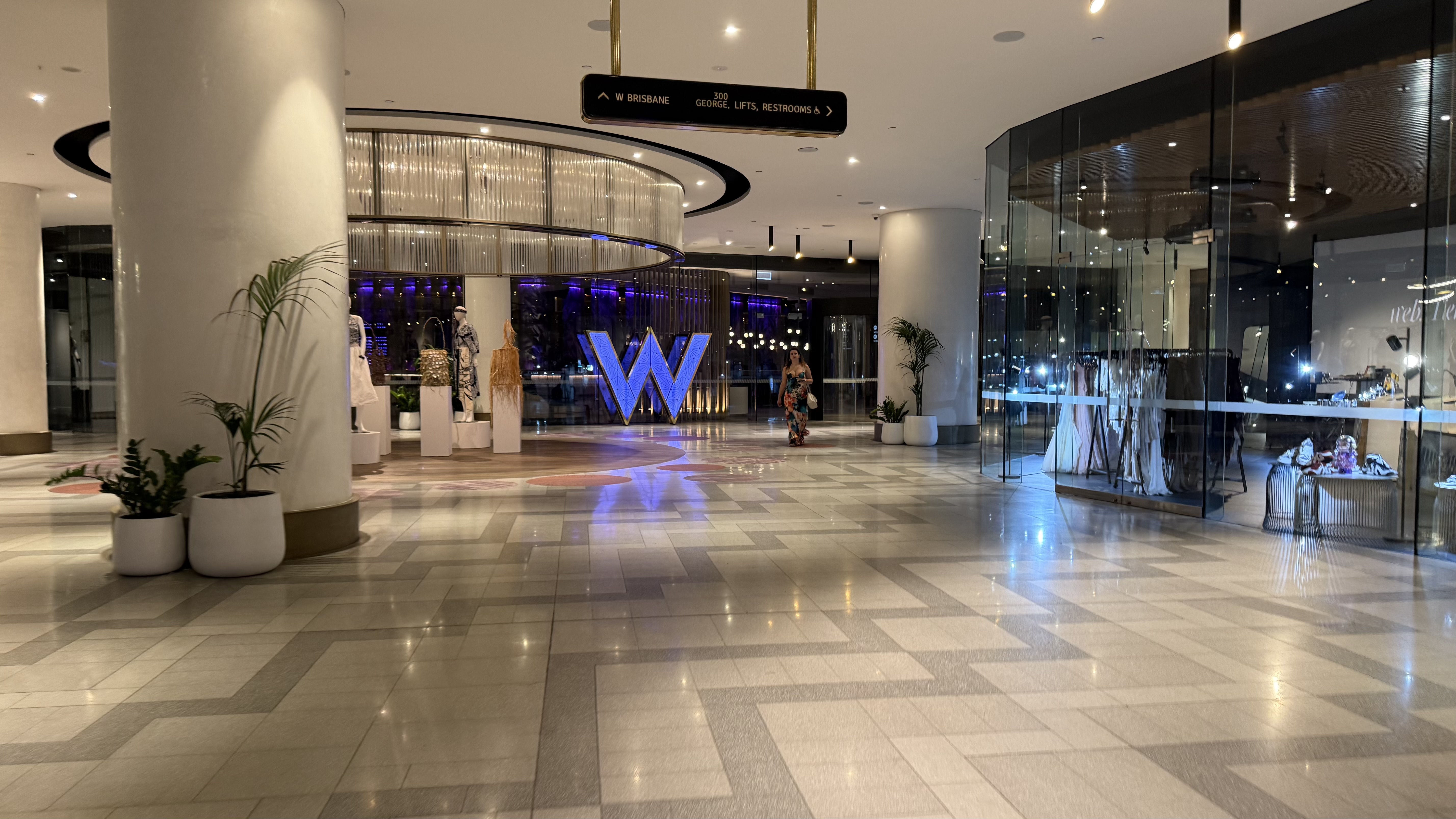 The glowing blue W sculpture and lobby signage from the mall entrance at night