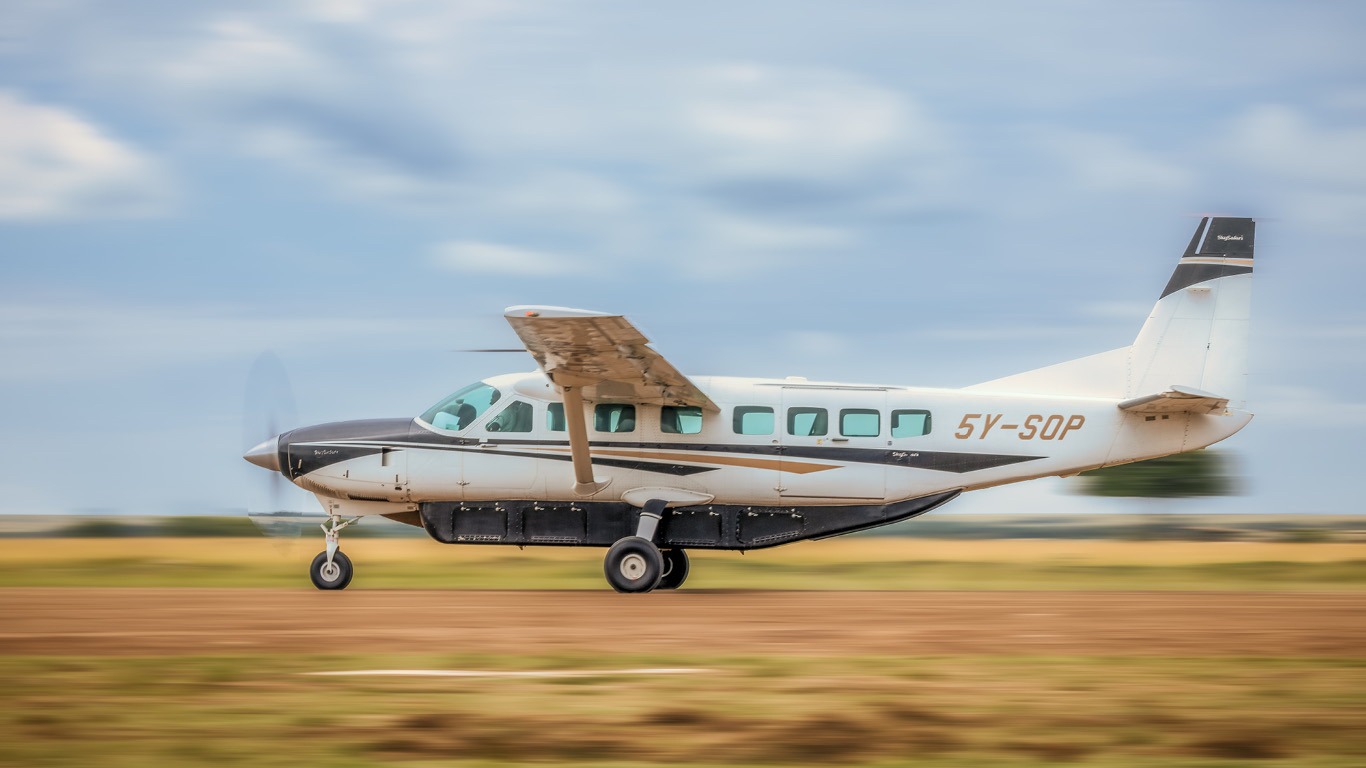 A bush plane taking off along a dirt runway in the East African savannah