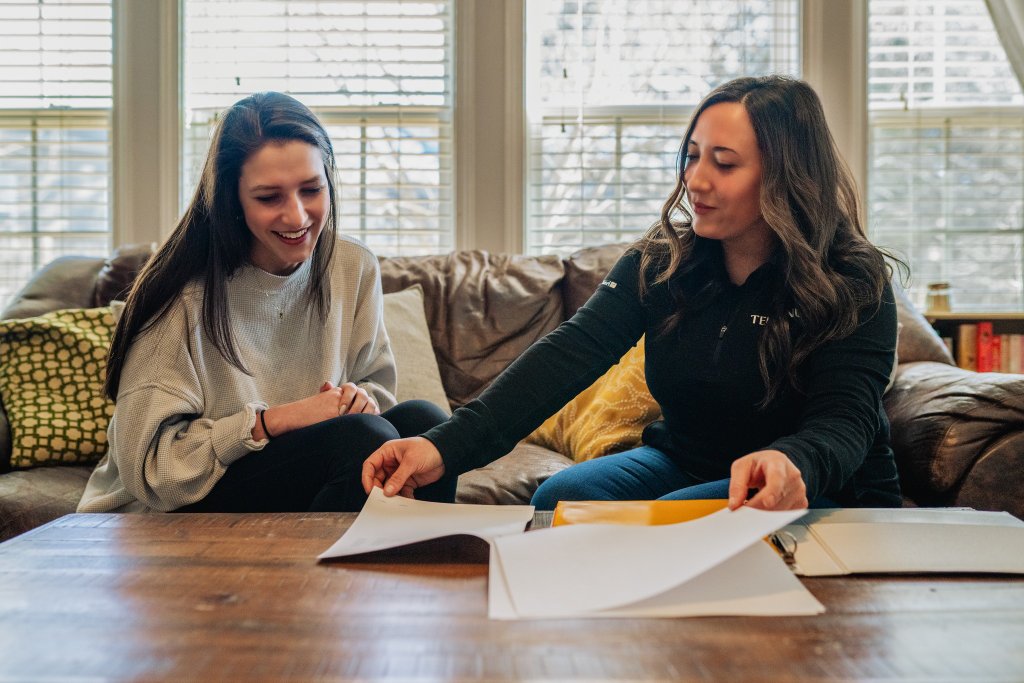 Why Homeowners Choose Terminus — personal in-home consultations Terminus Roofing team member meeting with a homeowner in her living room to review a roof estimate and insurance paperwork