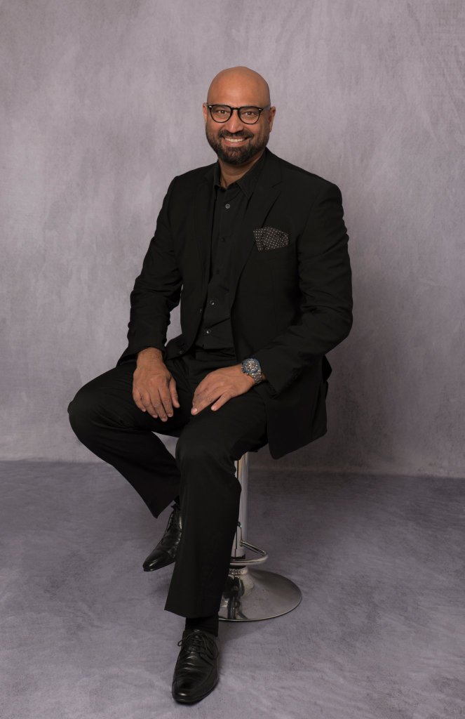 Professional LinkedIn headshot of a young male professional in grey suit, light grey background, friendly approachable smile