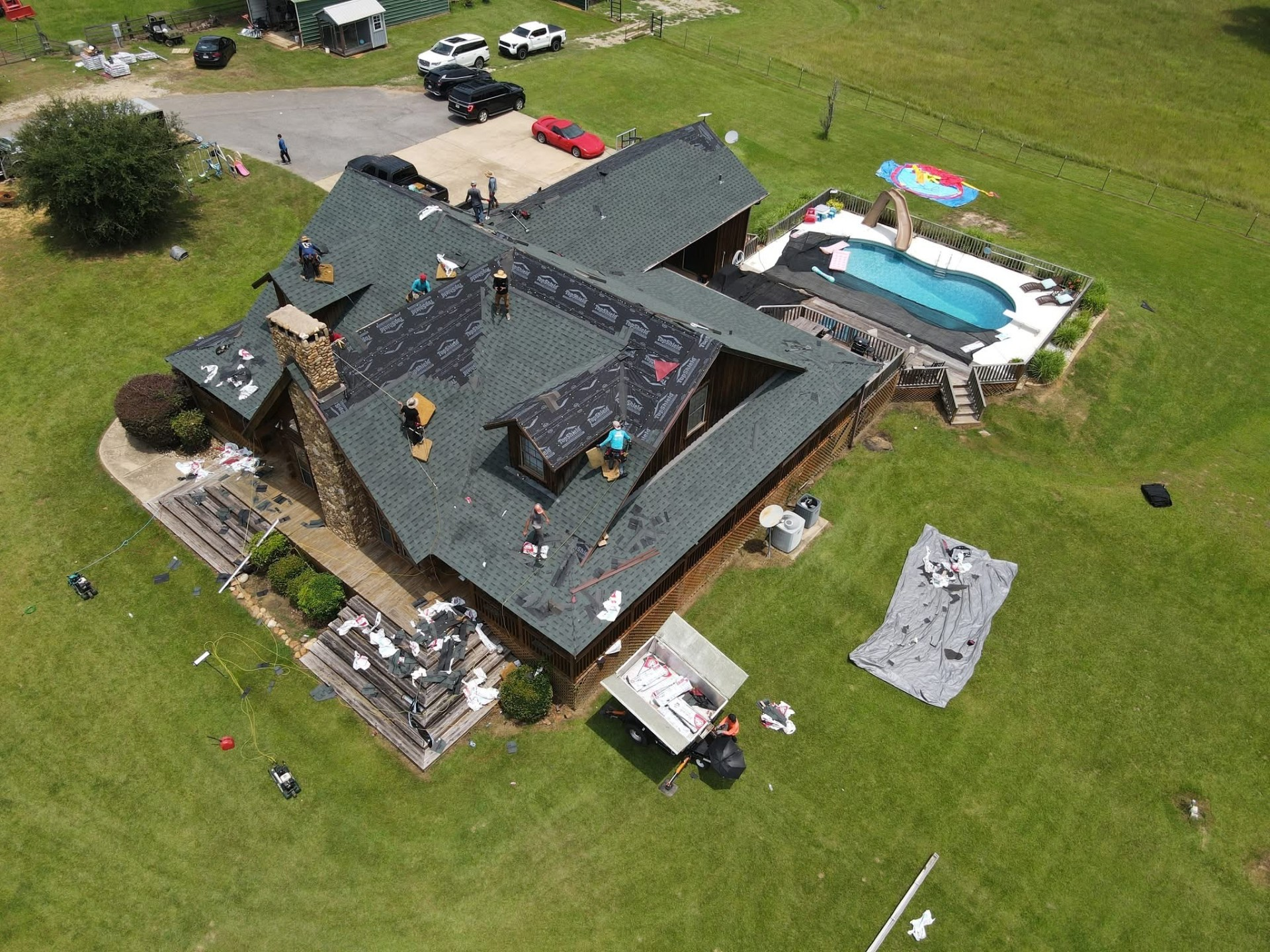 Aerial of log home roof replacement in progress with crew at work
