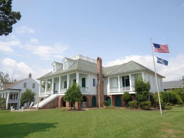 Two-story colonial home with white siding, brick foundation and wrap-around porch