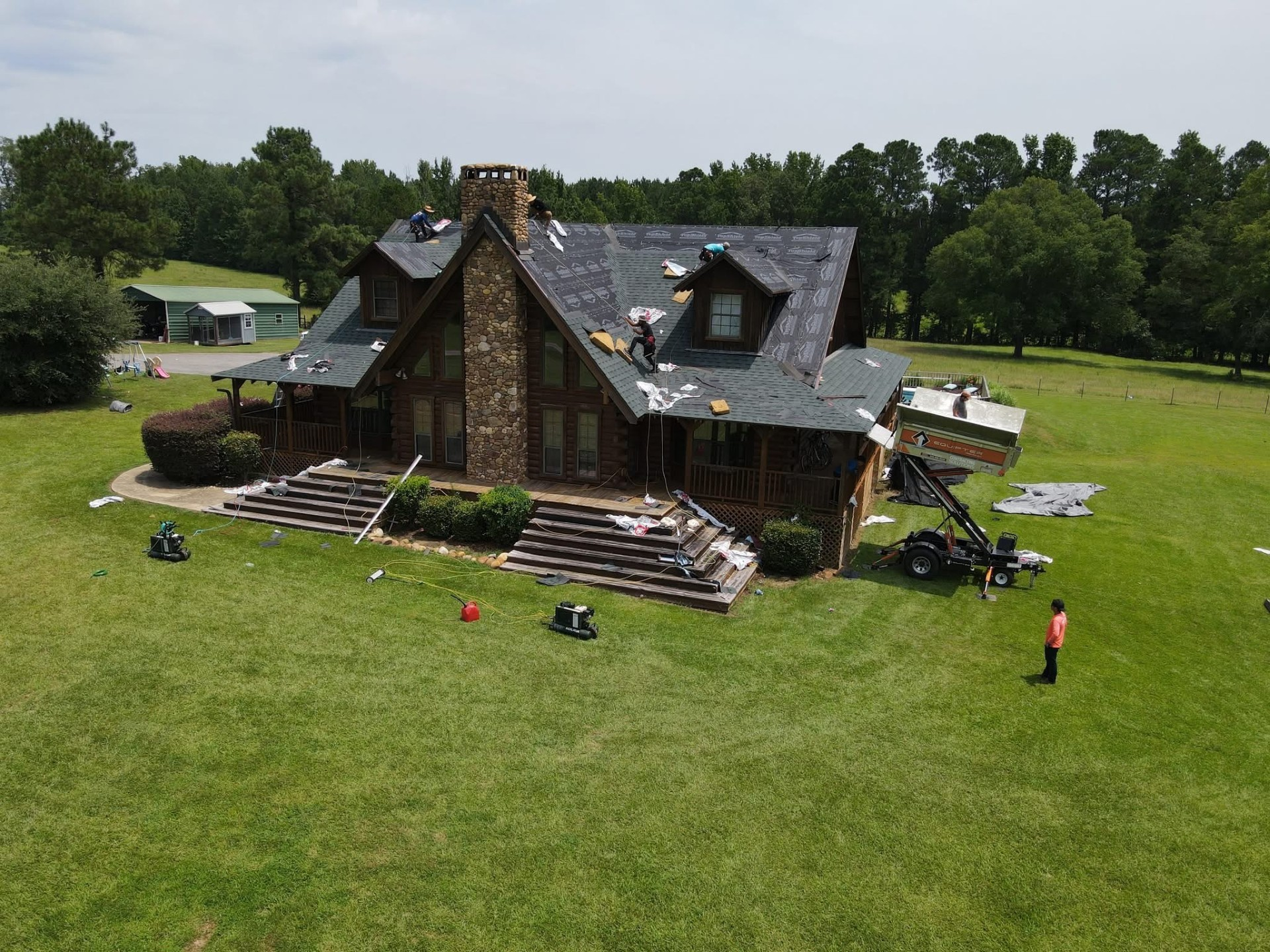 Aerial of wood-sided home mid-tear-off with TopShield underlayment exposed