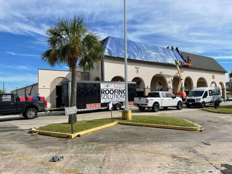 Commercial building with arched facade, blue tarp on roof and orange lift at work
