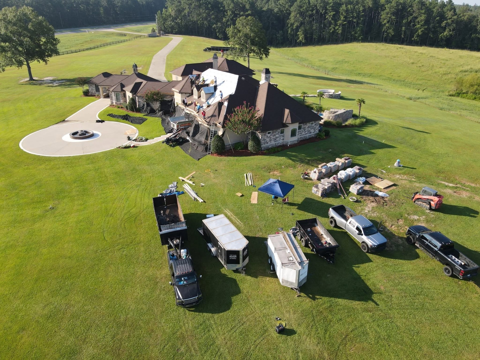 Aerial of estate roof replacement with shingle pallets and canopy staged on the lawn