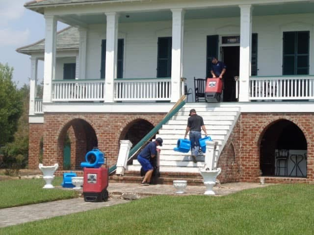 Crew carrying drying equipment into a columned brick-base home after water damage