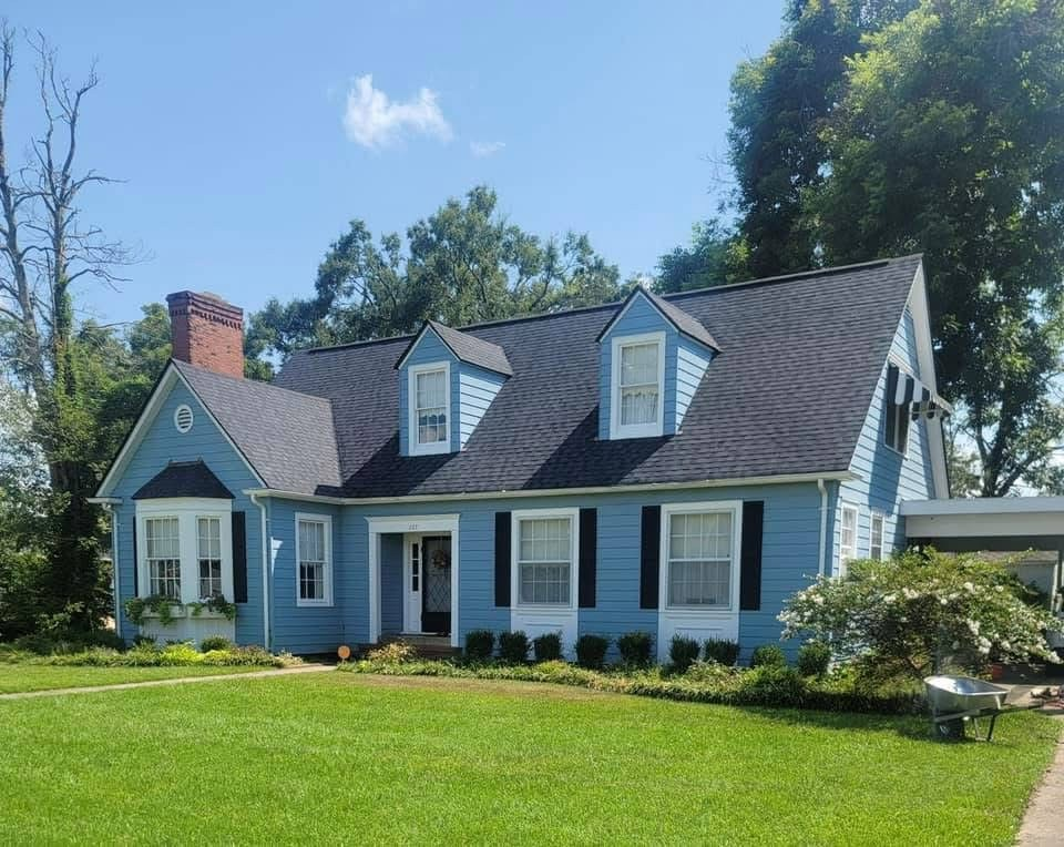 Light-blue siding colonial with charcoal roof, bay window and carport