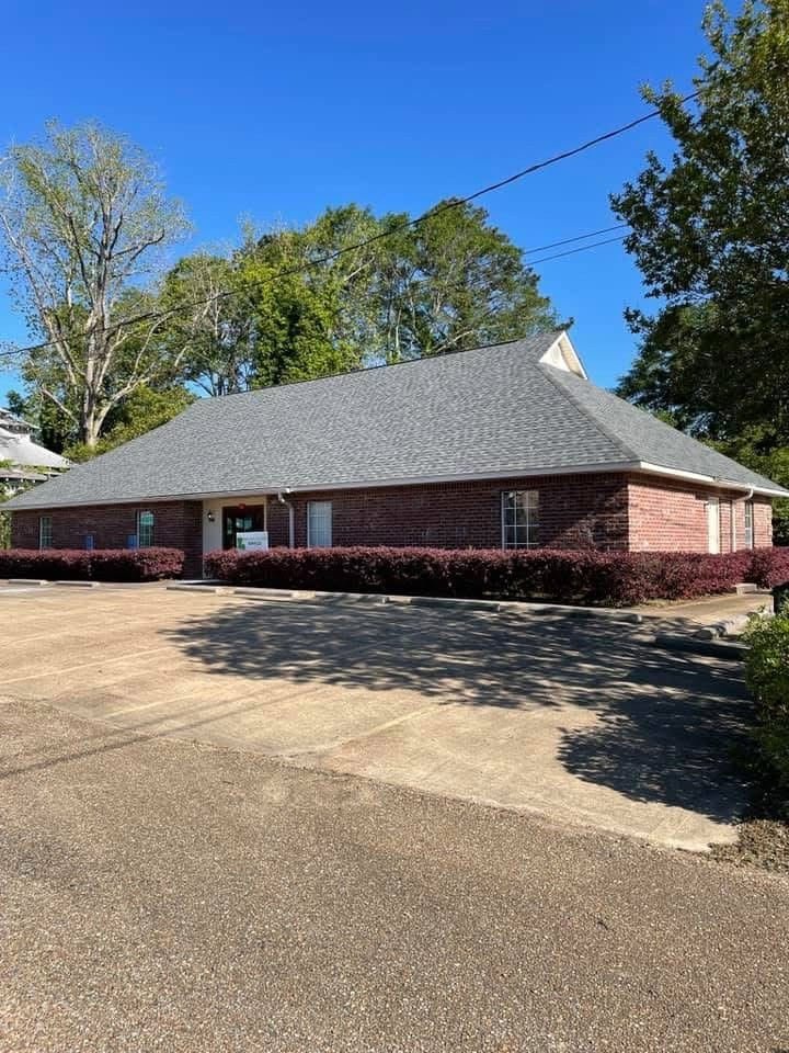Single-story red brick commercial building with grey hip roof and landscaped front