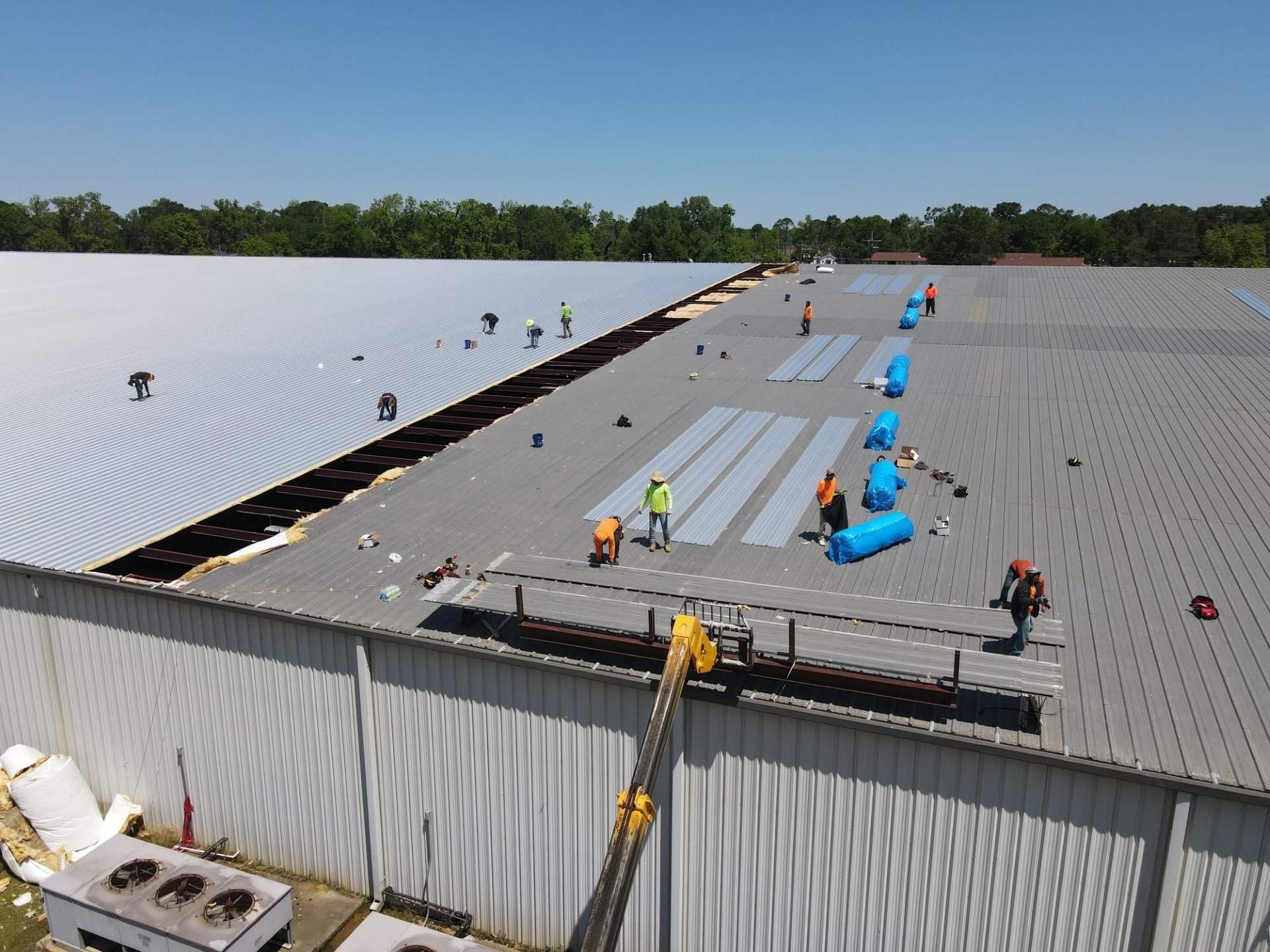Aerial of commercial re-roof with crew installing panels and boom lift staged