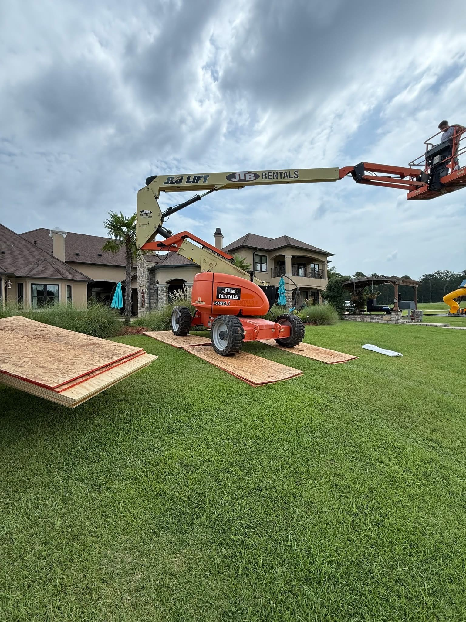 JLG boom lift accessing the roofline with plywood protecting the lawn