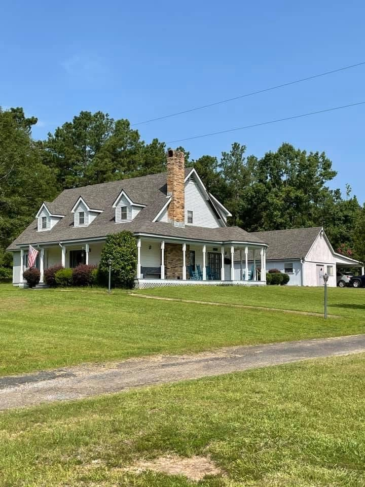 Two-story white colonial with steep grey roof, brick chimney and wrap-around porch