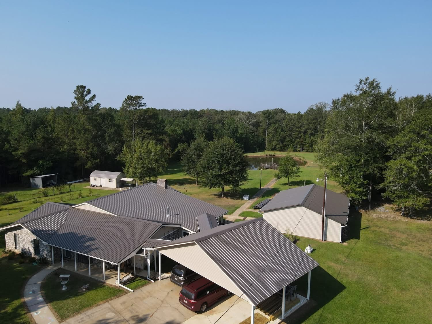 Aerial of home with dark brown metal roof, carport and pond beyond