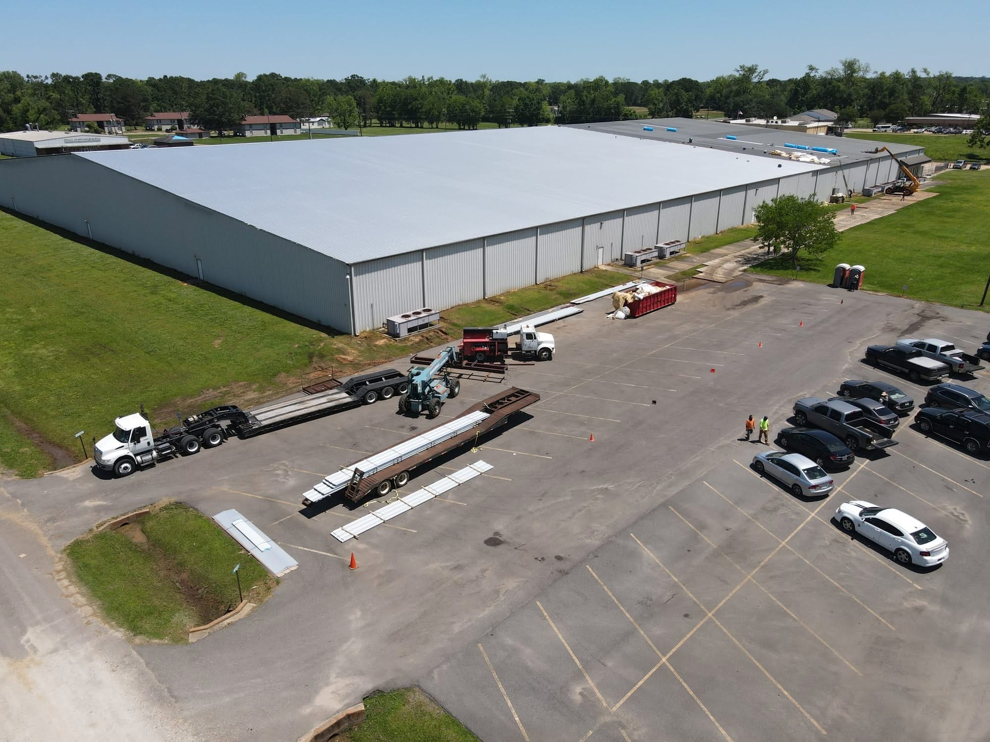 Warehouse re-roof with boom lift and panel staging in the lot below