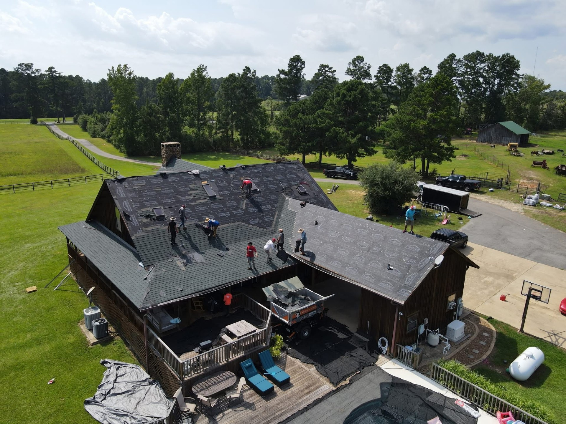 Aerial of single-story home mid-re-roof with dump trailer staged on the lawn