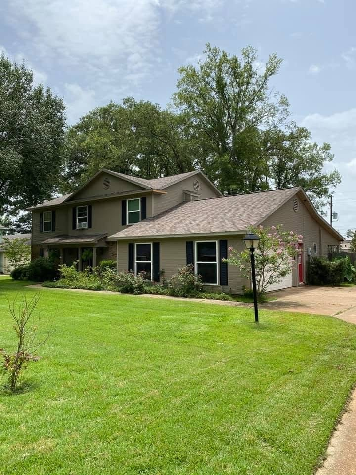 Two-story tan siding home with dark brown shingle roof and dormers