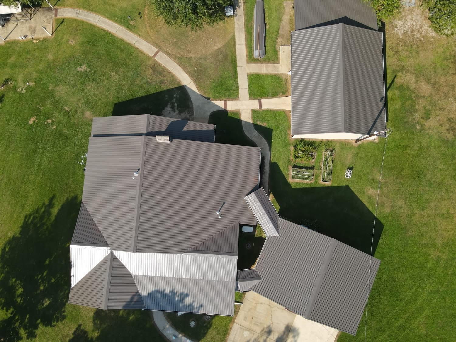 Aerial of estate with dark brown metal roofs on main house and detached building