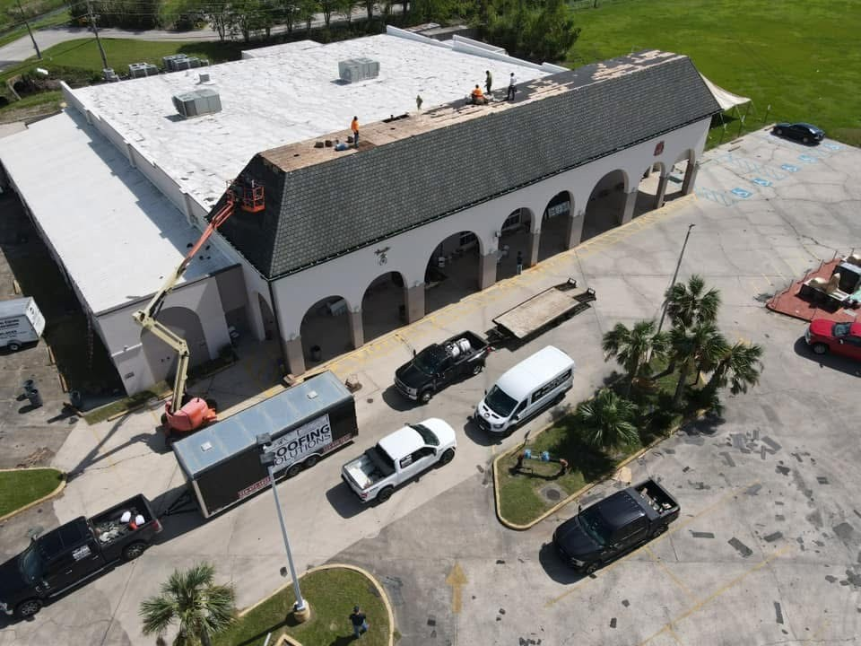 Aerial of arched commercial building with crew tearing off the pitched roof section