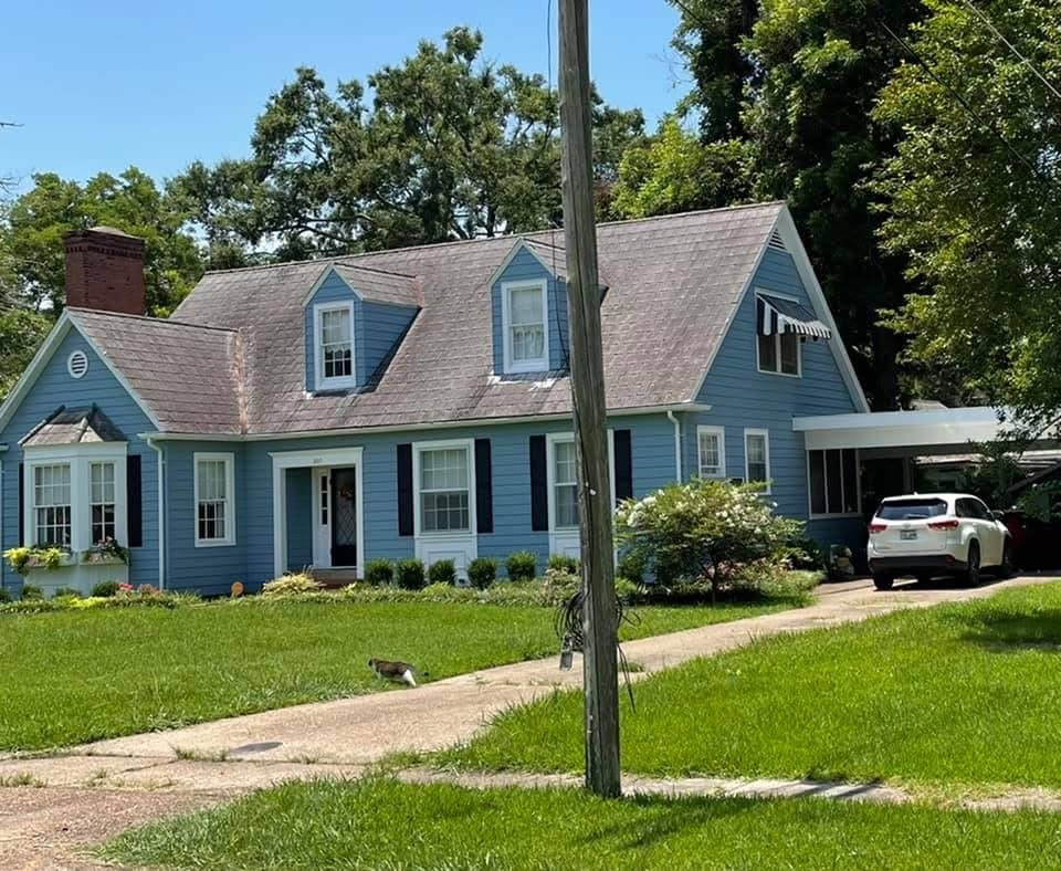 Two-story light-blue siding home with dormers, brick chimney and carport
