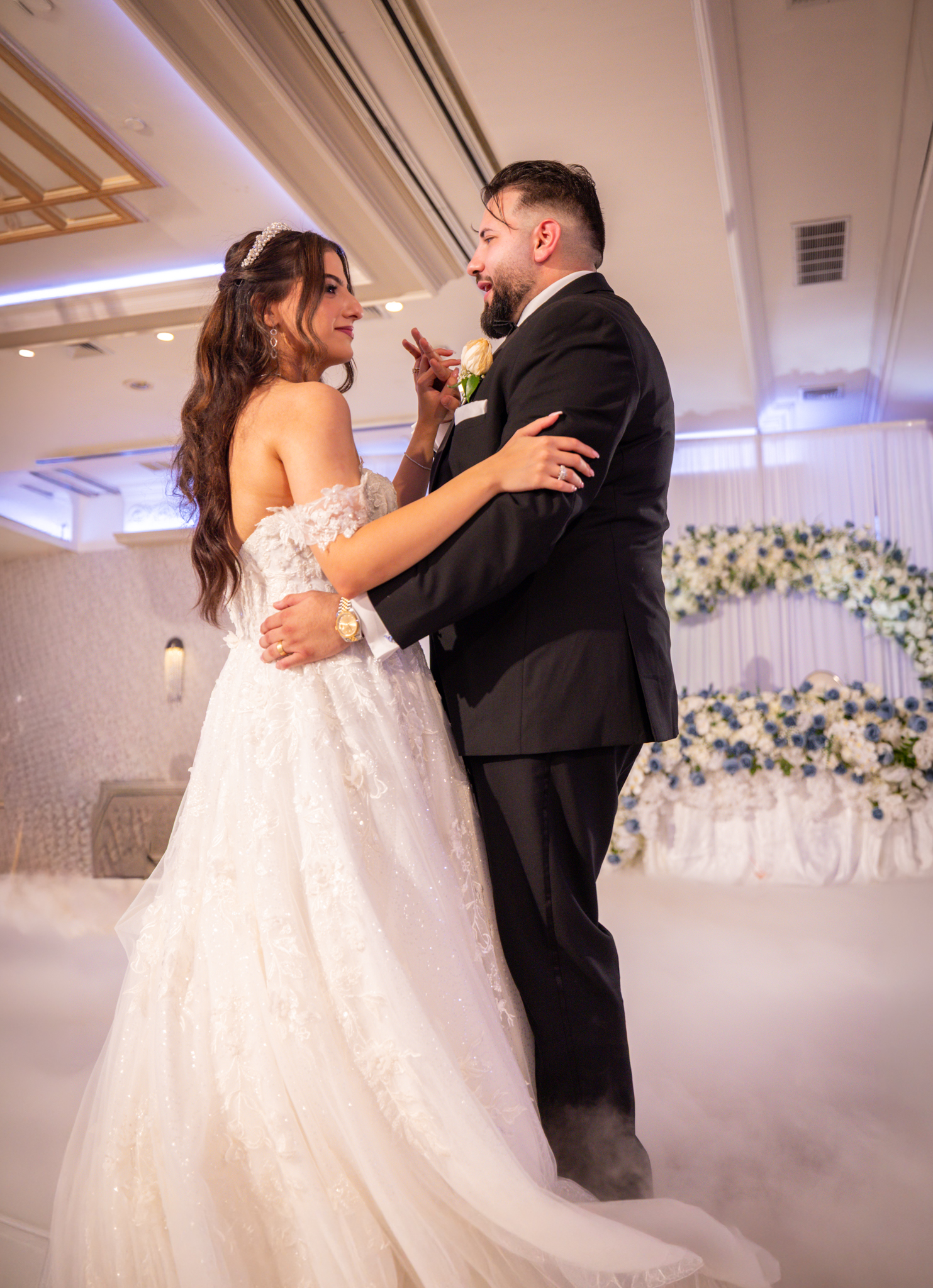 Bride and groom embracing on a fog-covered dance floor in front of a floral arch