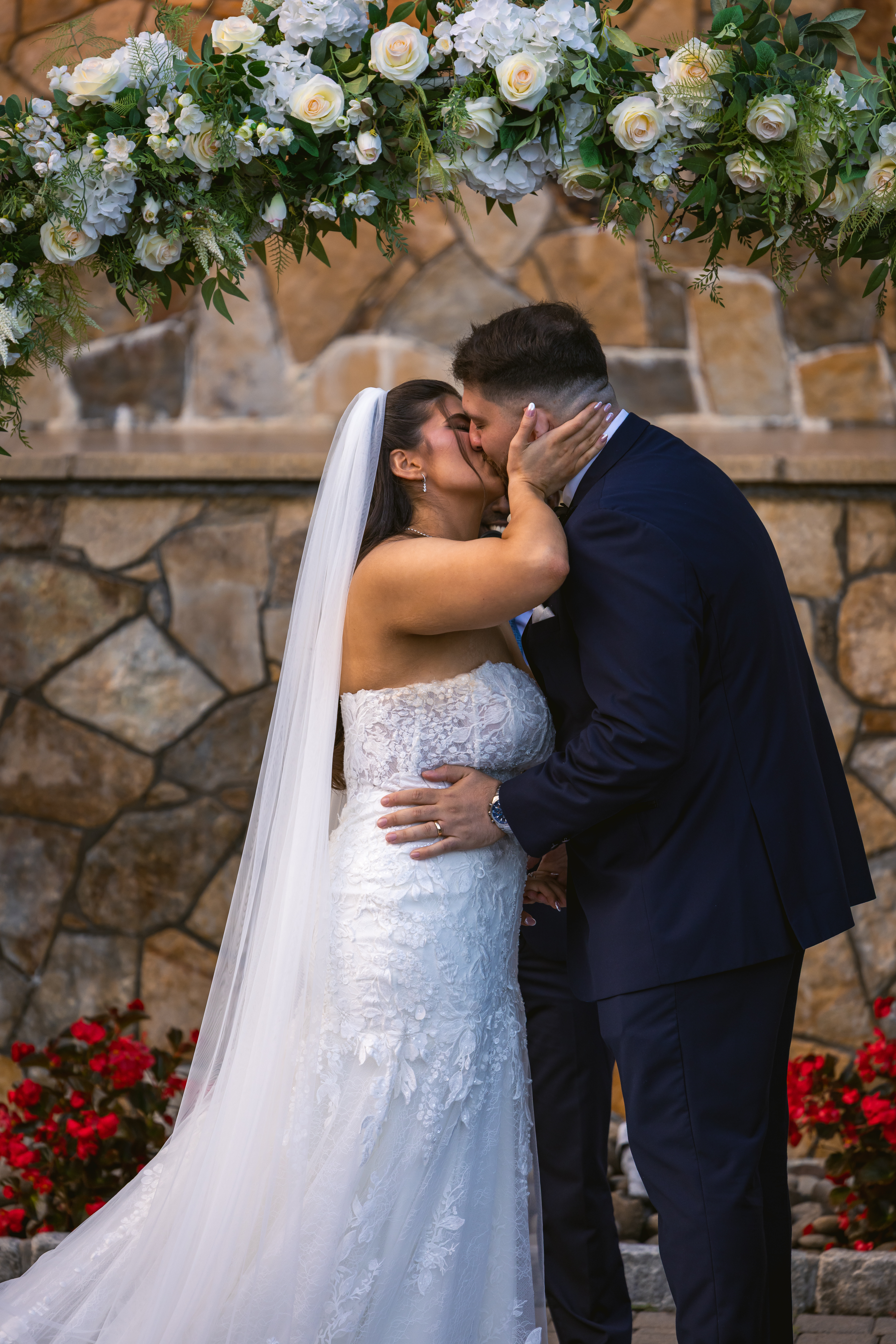 Bride and groom kissing in front of a white rose arch at their ceremony