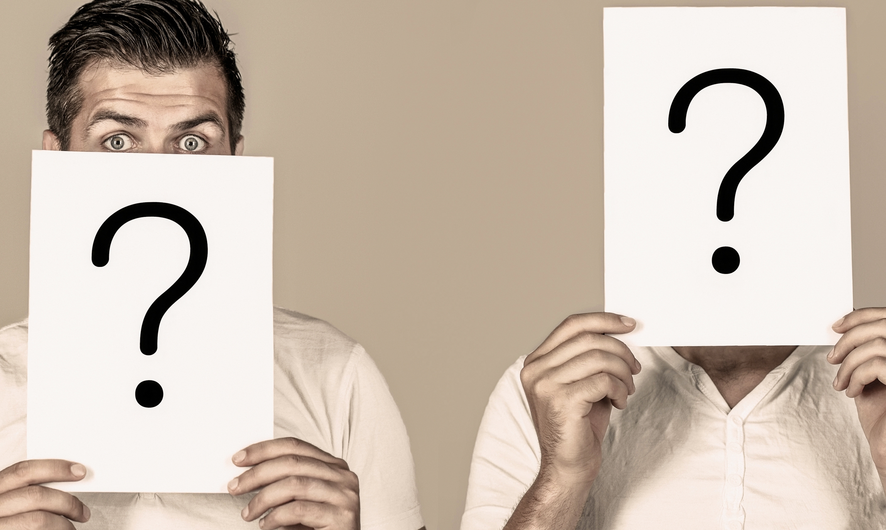 Two people holding up sheets of paper with question marks in front of their faces