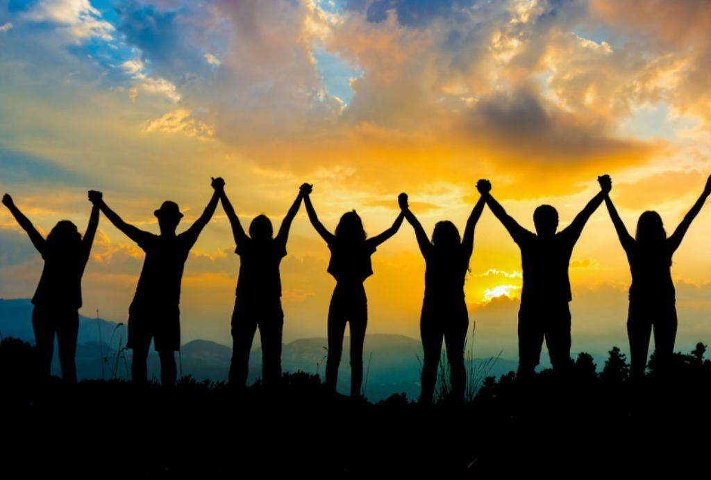 Silhouettes of people raising their hands together towards the sunset