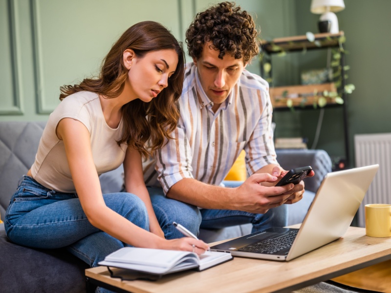 Couple researching donor conception options together at home with laptop and notebook