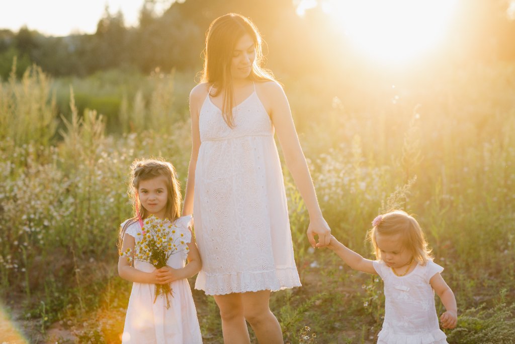 Solo mother walking through a sunlit meadow holding hands with her two young daughters