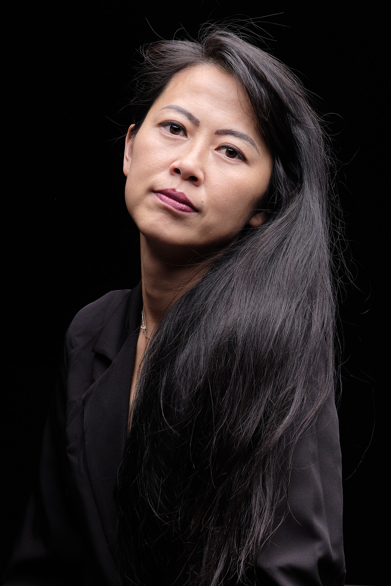 Studio portrait of woman with long dark hair in black jacket against black background