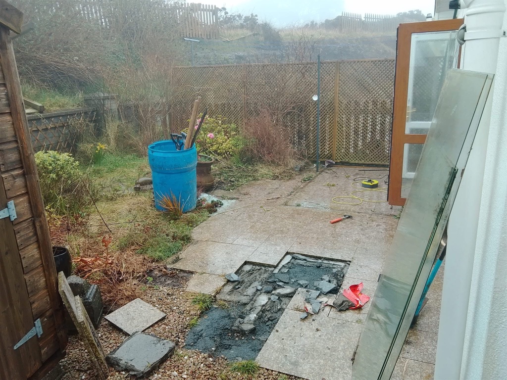Before patio installation — old broken slabs and overgrown garden