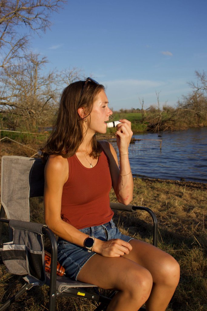 Woman applying lip balm by the water at golden hour