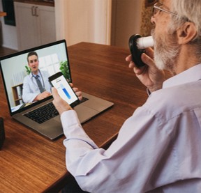Male patient measuring FEV₁ at home with live video coaching from a respiratory specialist on a laptop