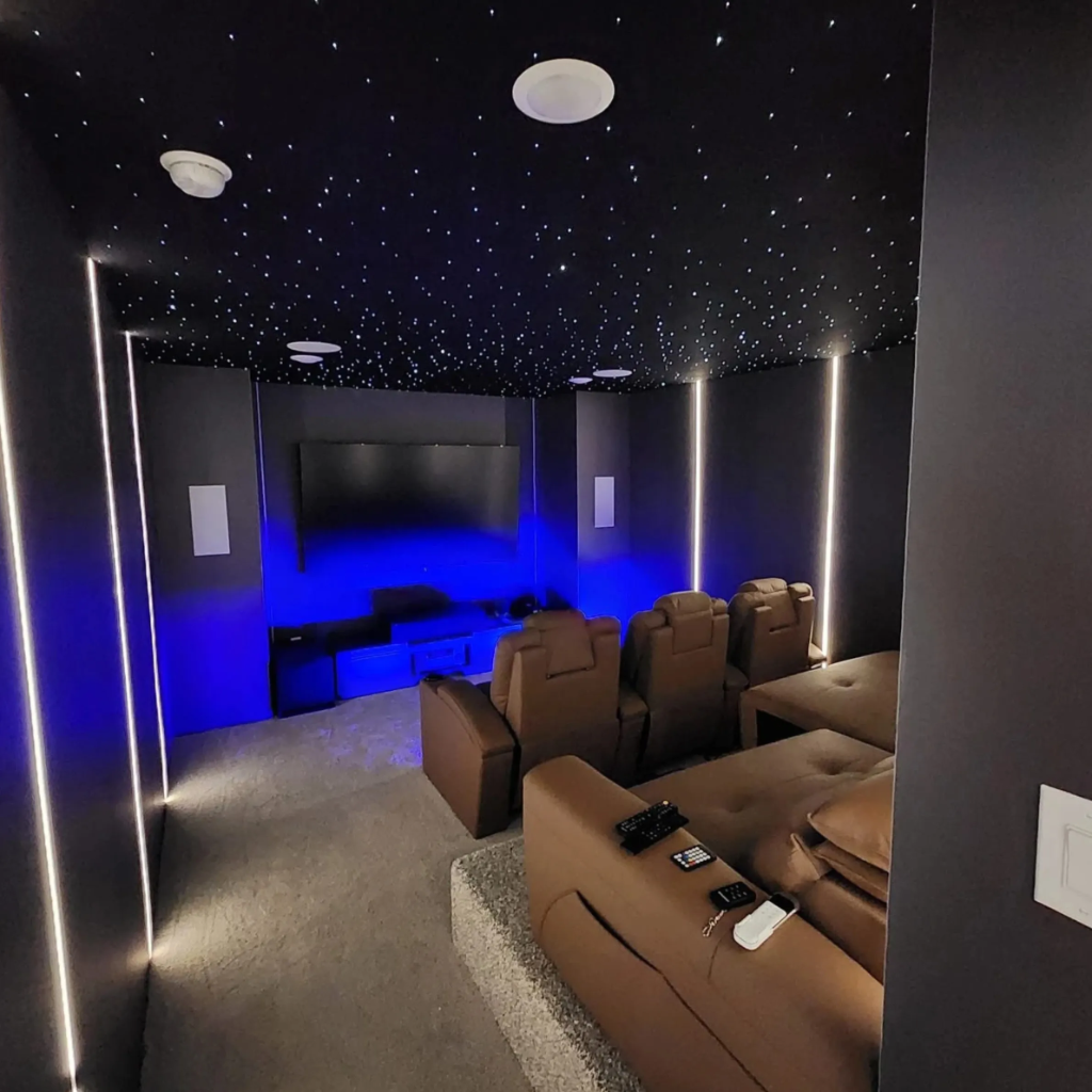 Luxurious home theater room with fiber optic starry ceiling, blue LED strip lighting, reclining seats, and large projection screen by 448 Developments DFW