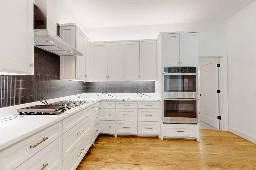 White shaker cabinet kitchen remodel with dark vertical tile backsplash, quartz countertops and stainless steel double oven in DFW
