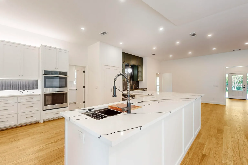 Open concept white kitchen remodel with large quartz waterfall island, hardwood floors and double wall oven in Dallas Texas