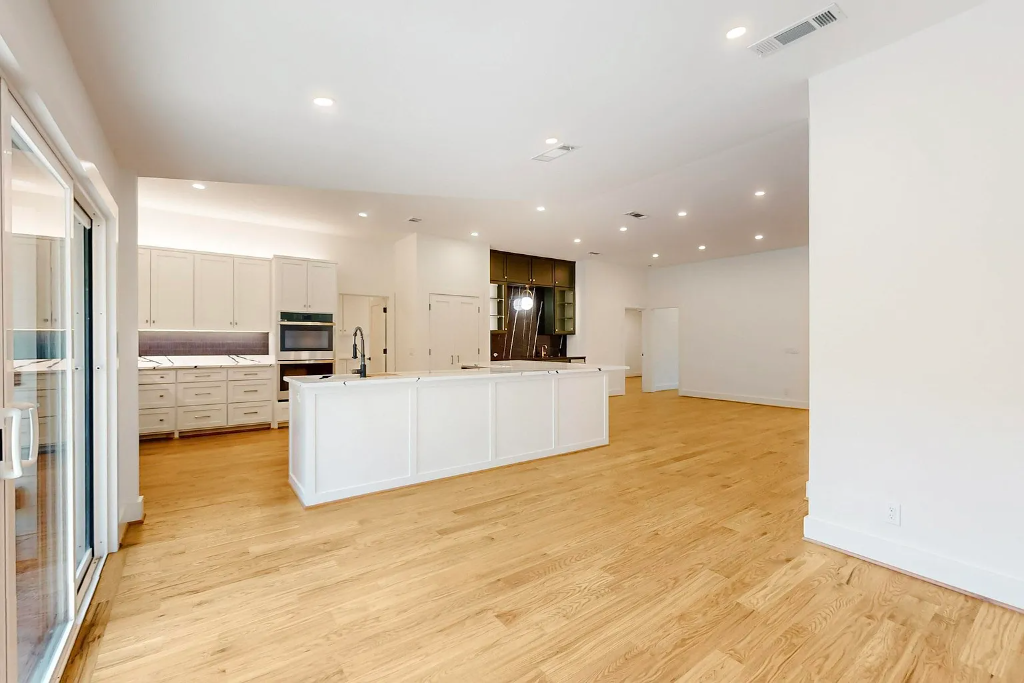 Open plan white kitchen with large peninsula island, recessed lighting, hardwood floors and sliding glass door access in Dallas