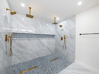 Luxury walk-in shower remodel with full marble tile walls, dual ceiling rain heads, built-in shelf, mosaic floor and gold fixtures in DFW Texas