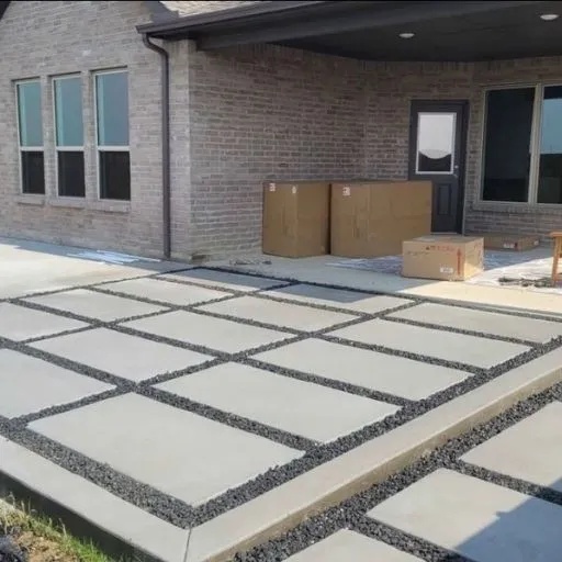 A contemporary concrete patio design featuring large square pavers separated by dark gravel inlays, professionally installed for a modern backyard in Dallas. Expert DFW concrete contractor services.