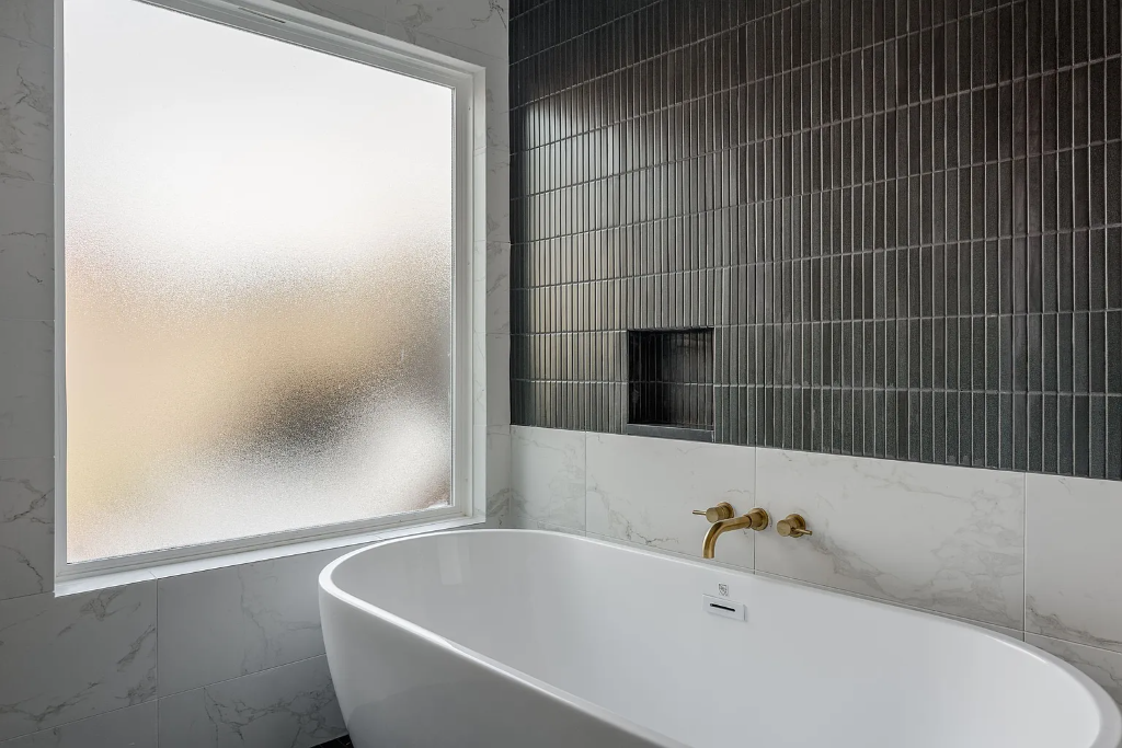 Luxury bathroom remodel with freestanding soaking tub, dark stacked tile accent wall, gold wall-mount faucet and marble tile in DFW