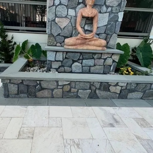 Beautifully crafted stone masonry wall incorporating a serene water feature and Buddha statue amidst lush greenery, demonstrating expert landscape and hardscape design in the Dallas-Fort Worth region.
