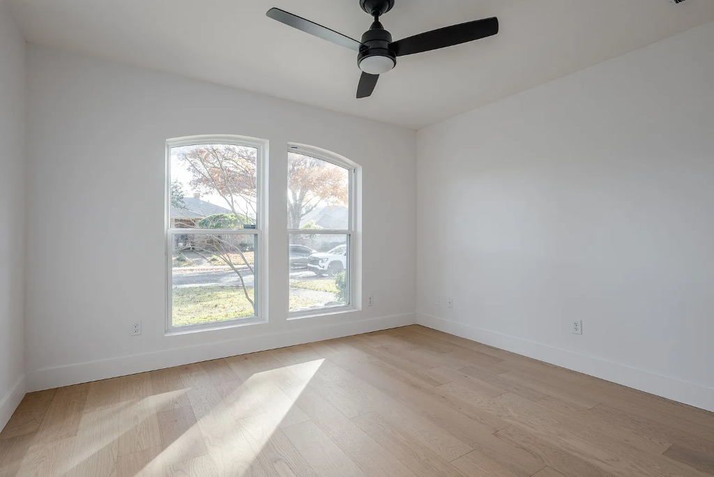 Bright bedroom featuring newly installed light hardwood flooring, white walls, and two elegant arched windows flooding the space with natural light by 448 Developments Dallas Texas
