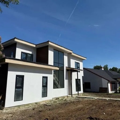 A striking contemporary home exterior with white stucco, dark accents, and large windows, part of a new construction project in Dallas, showcasing modern architecture.
