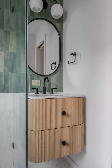 Contemporary bathroom remodel with floating wood vanity, sage green zellige tile, oval black-framed mirror and globe pendant lights in Dallas