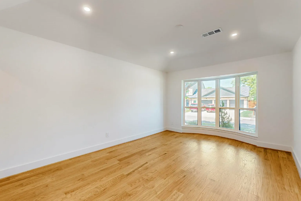 Large room showcasing newly finished light hardwood flooring and a prominent bay window with neighborhood views in a Dallas Texas home renovation by 448 Developments