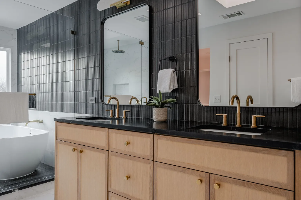 Bathroom renovation with light oak double vanity, black granite countertop, dark vertical stacked tile backsplash and gold fixtures in Dallas TX