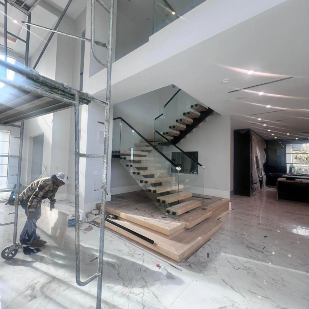 Large modern floating wood staircase with frameless glass balustrade and black hardware in open-concept DFW home by 448 Developments