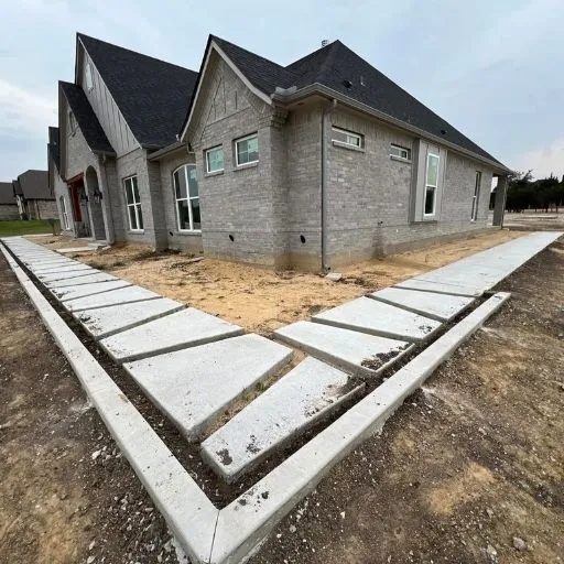 Modern concrete pathway and stepping stone installation leading to a contemporary brick residence, showcasing precision concrete and masonry craftsmanship in Dallas.