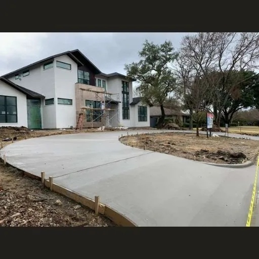 A newly poured, curving concrete driveway leading to a modern luxury home under construction in Dallas, showcasing expert driveway design and installation.