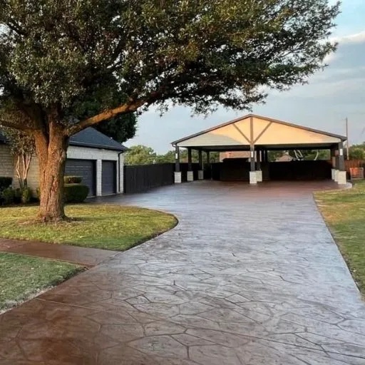 An impressive stamped concrete driveway leading to a large, covered carport structure, demonstrating custom concrete and outdoor living solutions in the DFW region.
